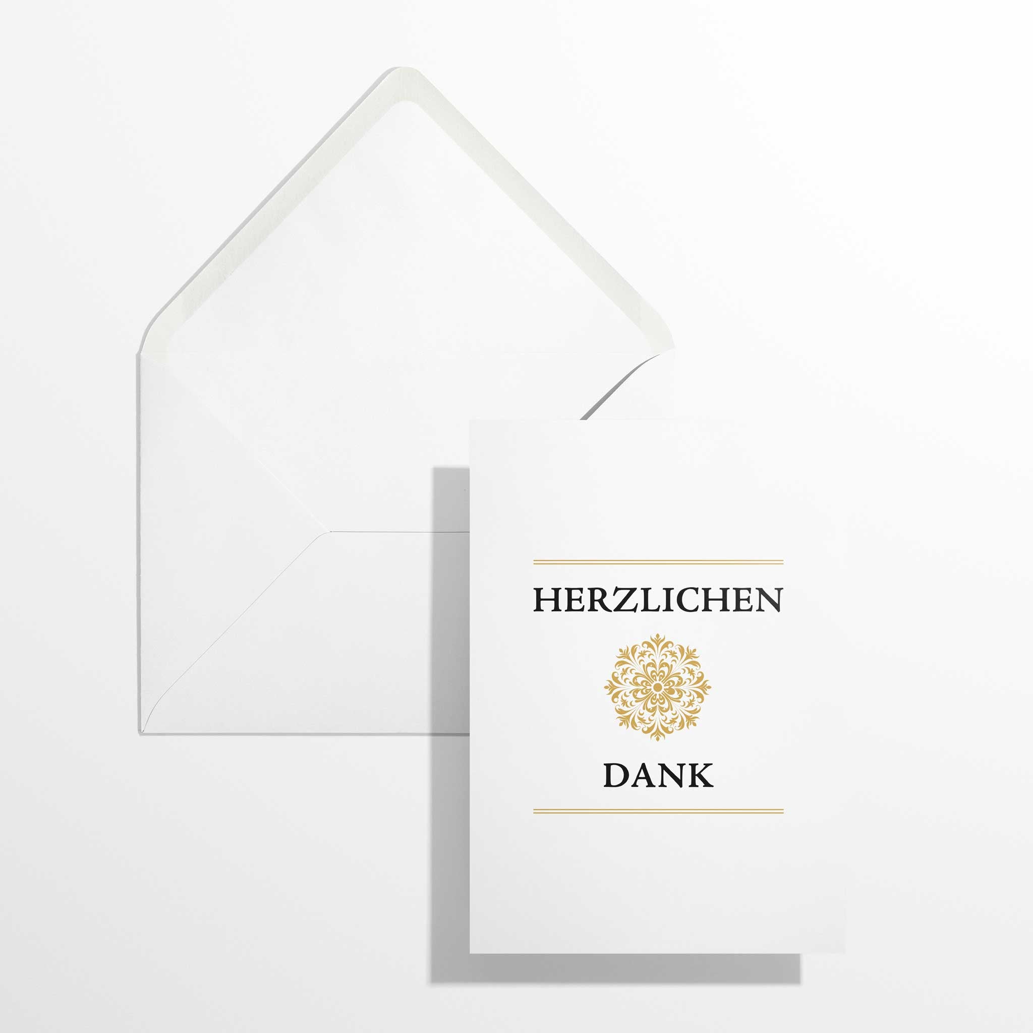 Elegante Dankeskarte mit Goldornament im Format B6 flach liegend neben dem geöffneten, naturweißen Premium-Briefumschlag mit klassisch spitzer Verschlussklappe.