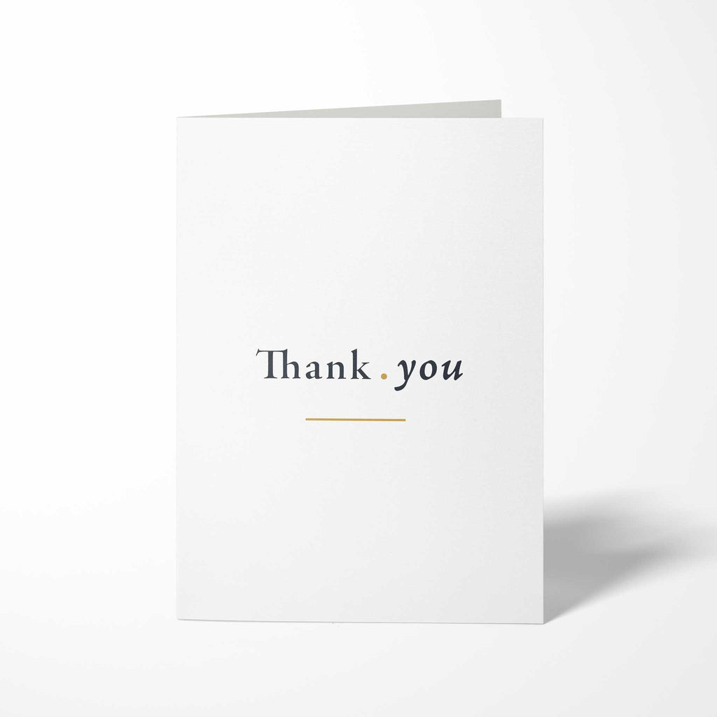Vorderansicht der hochkant gefalteten, weißen B6 Dankeskarte mit dem Schriftzug Thank you auf einer Linie, getrennt durch einen Goldpunkt und unterstrichen von einer Goldlinie.