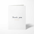 Vorderansicht der hochkant gefalteten, weißen B6 Dankeskarte mit dem Schriftzug Thank you auf einer Linie, getrennt durch einen Goldpunkt und unterstrichen von einer Goldlinie.