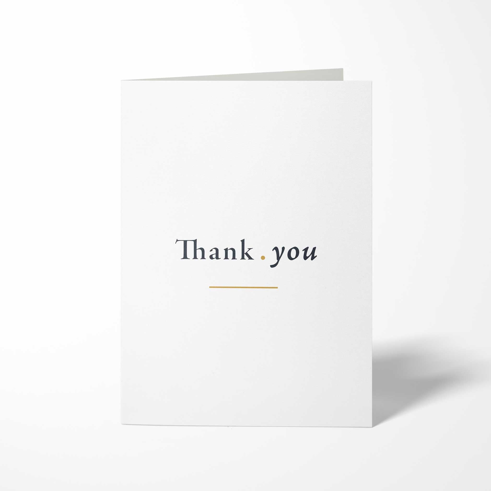 Vorderansicht der hochkant gefalteten, weißen B6 Dankeskarte mit dem Schriftzug Thank you auf einer Linie, getrennt durch einen Goldpunkt und unterstrichen von einer Goldlinie.