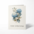 Vorderansicht der hochkant gefalteten B6 Geburtstagskarte mit einer klassischen botanischen Illustration zweier blauer Hortensienblüten und dem kursiven Schriftzug Zum Geburtstag.
