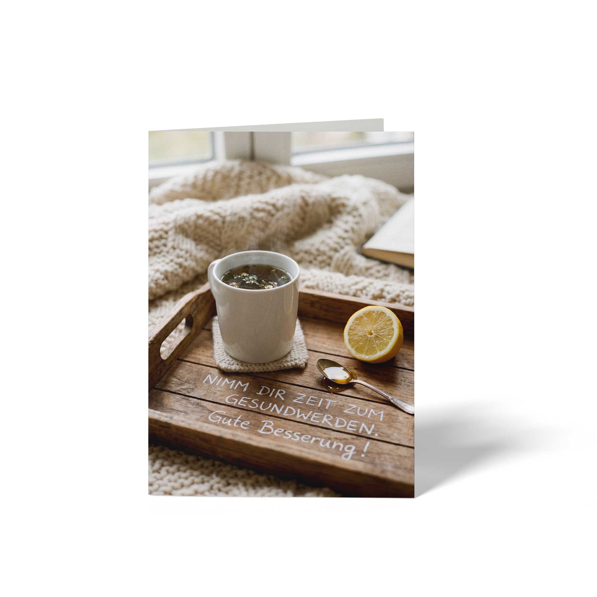 Vorderseite der geschlossenen A6 Genesungskarte von GHG Supplies. Gezeigt wird eine Tasse Kräutertee mit Zitrone und Honig auf einem Holztablett unter dem Spruch Nimm dir Zeit zum Gesundwerden. Gute Besserung!.