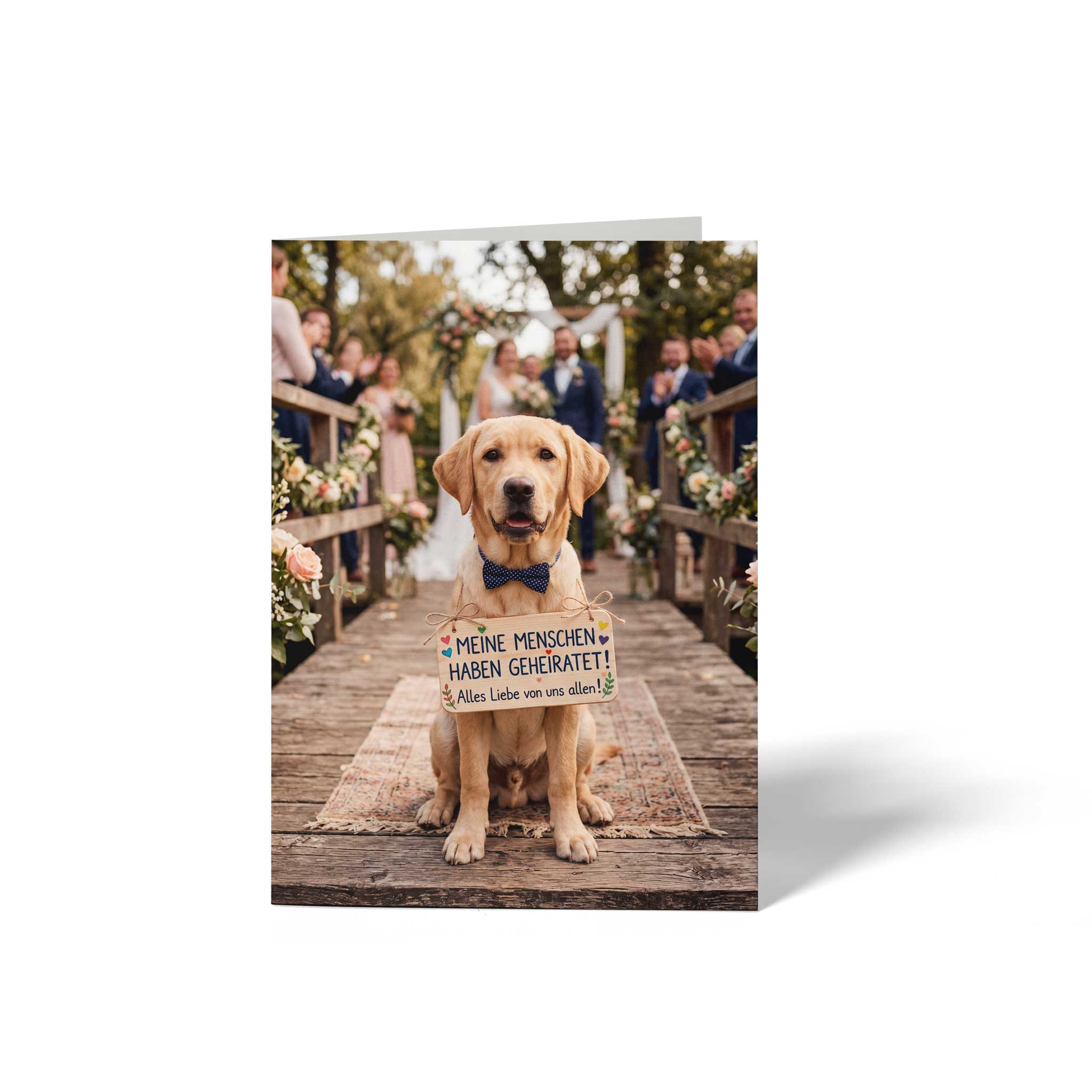 Vorderseite der geschlossenen A6 Hochzeitskarte von GHG Supplies. Ein goldener Labrador-Hund mit blauer Fliege trägt ein Holzschild mit der Aufschrift Meine Menschen haben geheiratet! Alles Liebe von uns allen! vor einer Hochzeitsgesellschaft.