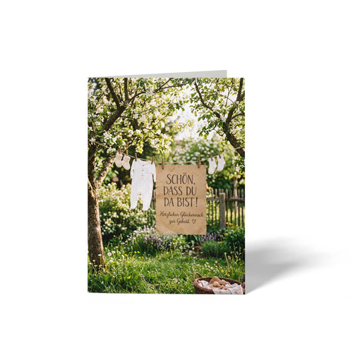 Vorderseite der geschlossenen A6 Babykarte von GHG Supplies. Eine Wäscheleine im blühenden Garten mit Strampler, Söckchen und Pergamentschild Schön dass du da bist, Herzlichen Glückwunsch zur Geburt.