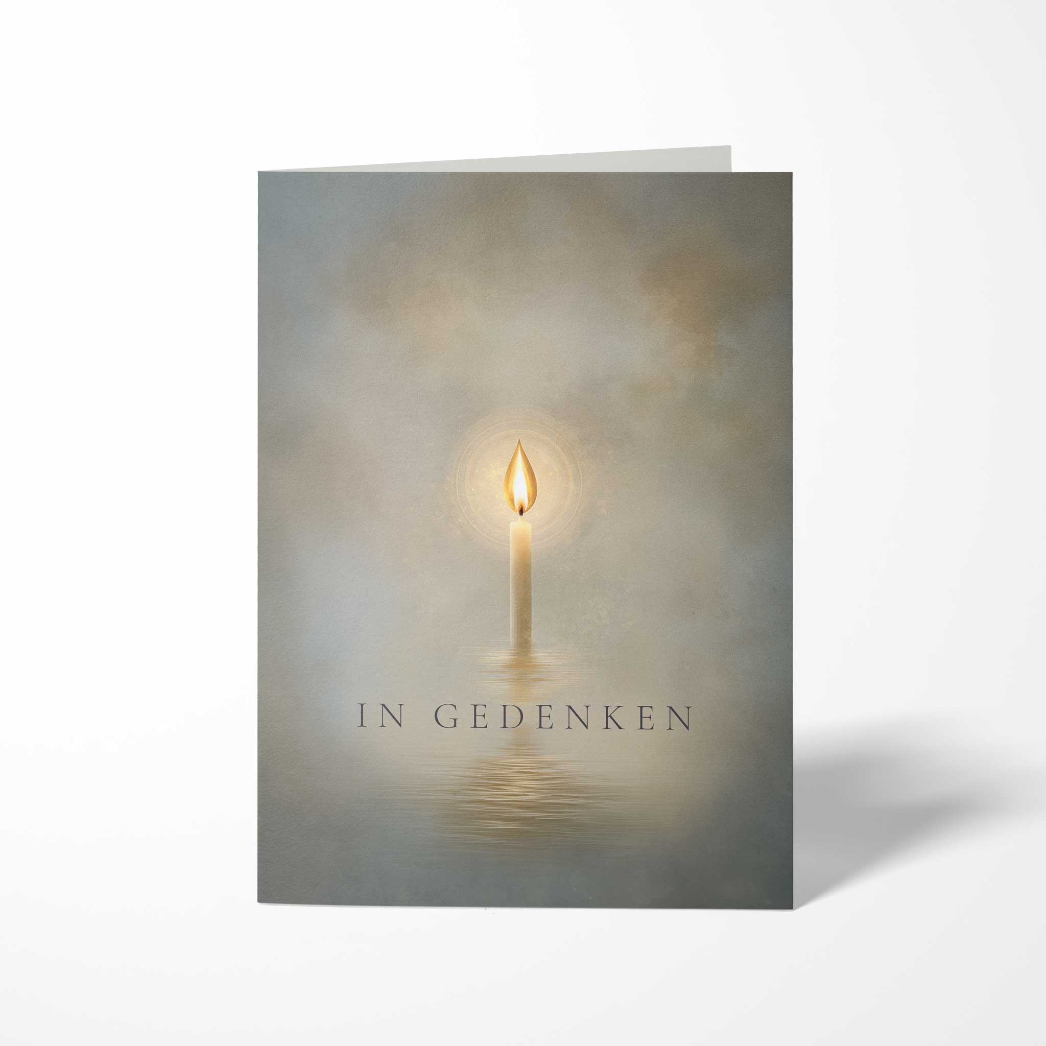 Vorderansicht der hochkant gefalteten B6 Trauerkarte mit einer brennenden Kerze im Nebel, deren Licht sich im Wasser spiegelt, und dem feinen Schriftzug IN GEDENKEN.
