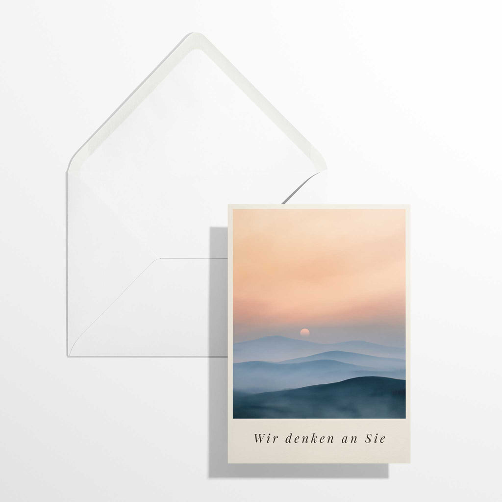 Atmosphärische Trauerkarte Sonnenuntergang im Format B6 flach liegend neben dem geöffneten, naturweißen Premium-Briefumschlag mit klassisch spitzer Verschlussklappe.