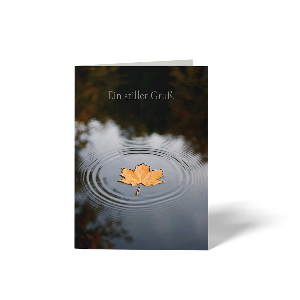 Vorderansicht der geschlossenen A6 Trauerkarte von GHG Supplies. Ein goldenes Herbstblatt liegt im Zentrum von feinen Wasserringen auf einer dunklen Wasseroberfläche unter dem Text Ein stiller Gruß.